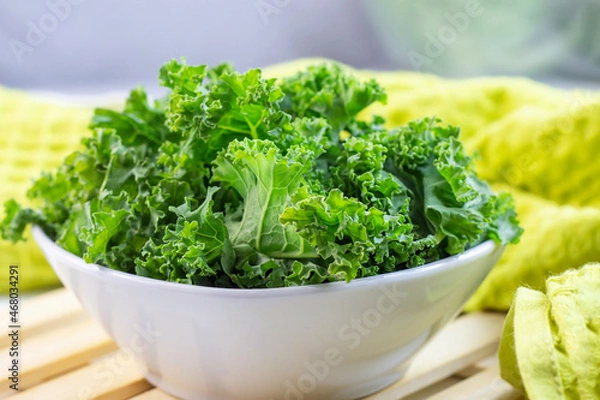 Fototapeta Fresh green curly cabbage or kale salad leaves cut in the bowl on light background on the table in the kitchen.