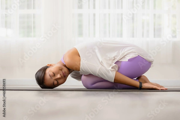 Fototapeta Asian woman working out in sportswear while doing yoga, seated in Child exercise, Balasana stance.