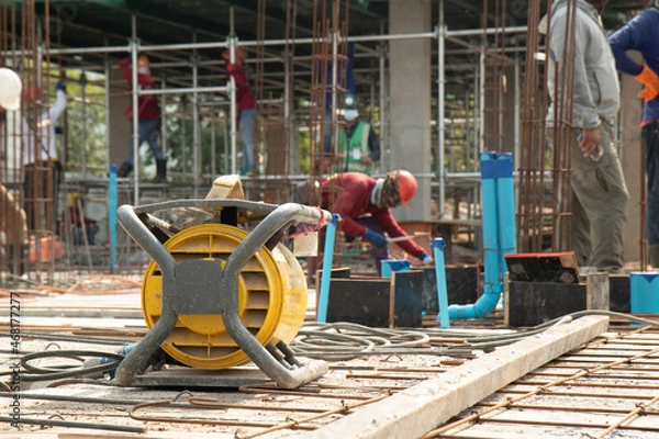 Fototapeta Yellow concrete vibrater on rebar for floor pouring frame in construction area, background with columnar and building condition during construction.