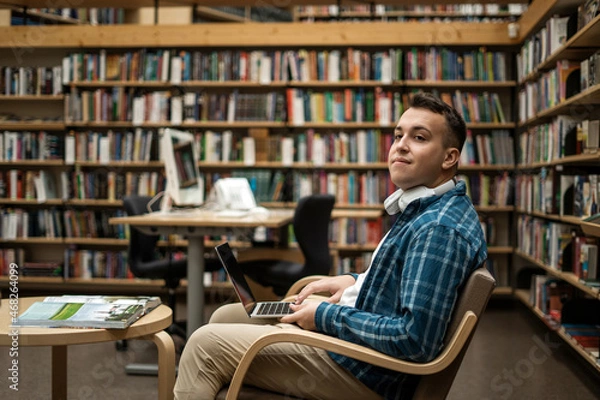 Obraz College break. Wireless headphones listening to an audiobook.  Male online education via the Internet on the school's website. The student is in the library.