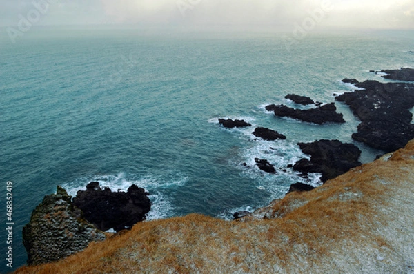 Obraz cliff edge and black basalt rocks in the blue sea with fog in the background, Lóndrangar, Iceland