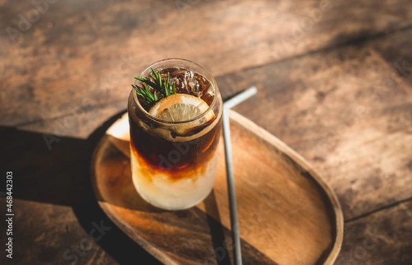 Fototapeta Top view of ice coffee with lemon and mix soda on wood rustic. A glass of americano mixed with craft soda and lemonade juice. Sparkling mixed beverage.