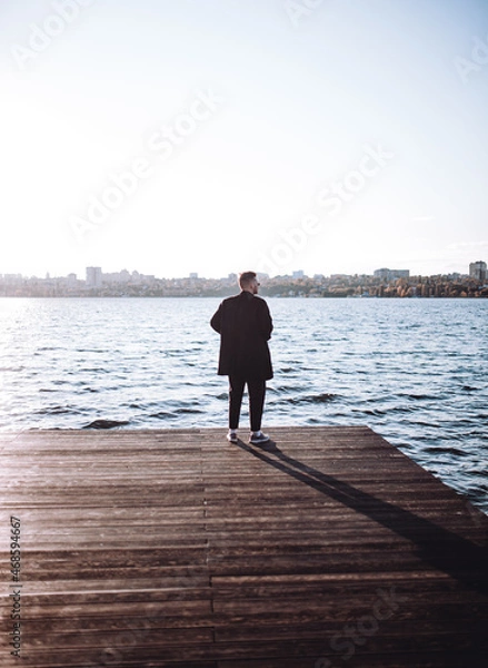 Fototapeta a young guy with a beard looks melancholically at the view of the lake