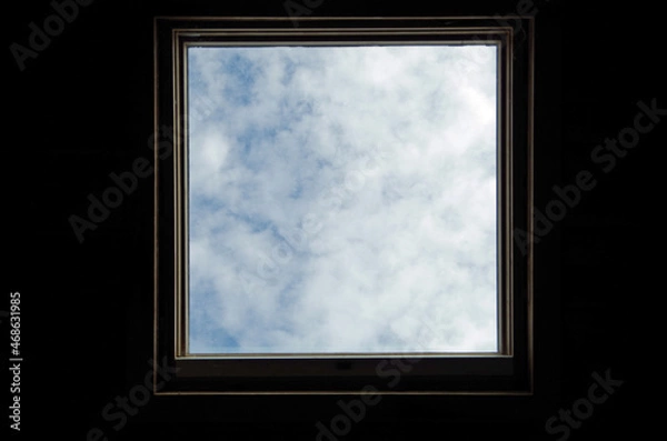 Fototapeta Skylight surrounded by darkness. Blue sky and clouds. Conceptual metaphor. 