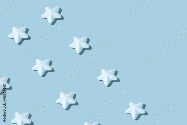 Fototapeta Christmas creative pattern made of sparkling white stars against ice blue background. Winter holidays and New Year concept.