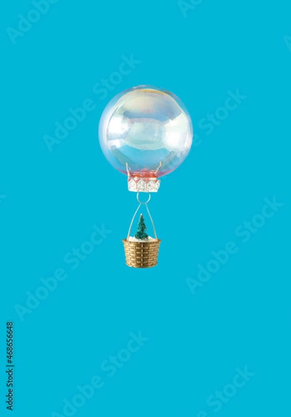 Fototapeta Christmas bauble flying with green Christmas tree with snow in the basket against sky blue background. Creative winter holidays and New Year concept.