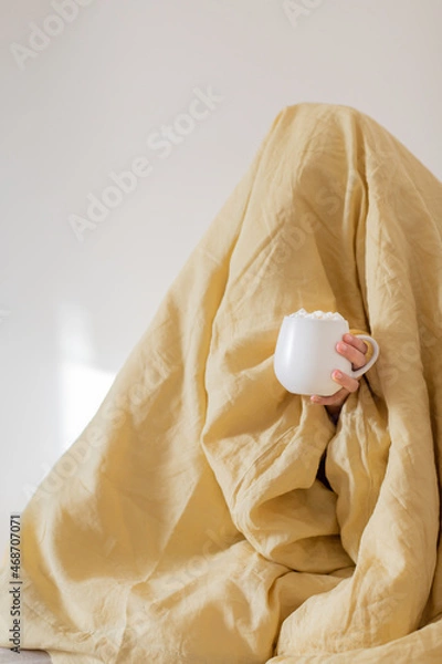 Fototapeta Woman under a yellow blanket with his head. A mug with marshmallows and a drink is on display outside. The concept of autumn and winter.