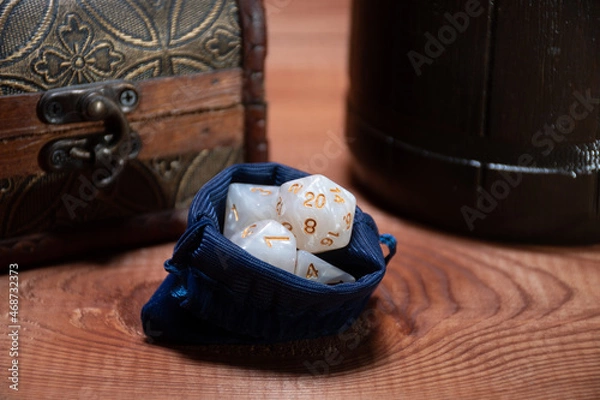Fototapeta A set of white polyhedral cubes for role-playing games lie in a blue storage bag next to a wooden box and a mug: the concept of board games