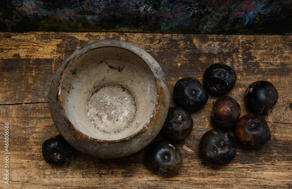 Fototapeta An old cast iron pot stands on a wooden board. Black rotten apples lie nearby. View from above