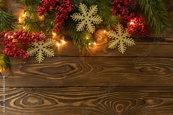 Fototapeta Christmas background. Nobilis fir branches, twigs with red berries, toy golden snowflakes on brown wooden planks. Copy space, flat lay, top view. Holiday, Xmas, New Year concept. Mockup
