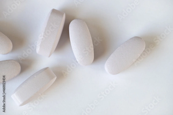 Fototapeta White or light grey long vitamins or pills on white background, macro, close-up, copy space, flatly. Nutritional supplements concept, health, vitamins, monochrome minimal style. Horizontal