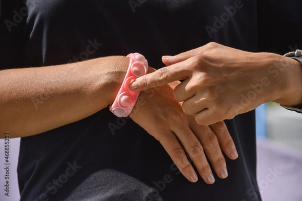 Fototapeta Close-up of a popit and simple dimple toy. A bracelet on a woman's hand in the form of a pink silicone anti-stress toy for children