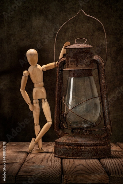 Fototapeta A wooden man and an old rusty kerosene lamp on a wooden table and an artistic background.