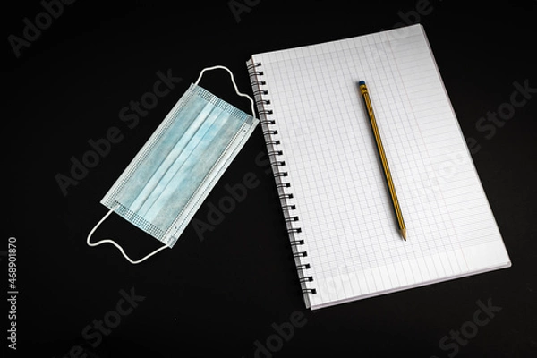 Fototapeta Blank notebook with pencil on black background with . Medical mask laying next to notebook. Work at home concept.