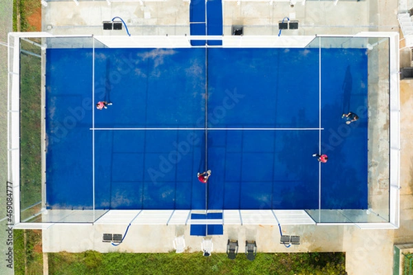 Obraz View from above, stunning aerial view of some people playing on a blue padel court. Padel is a mix between Tennis and Squash. It's usually played in doubles on an enclosed court.