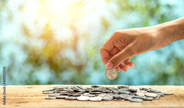 Fototapeta Woman hand putting coin dollar on coins stack with green bokeh background, investment concept.