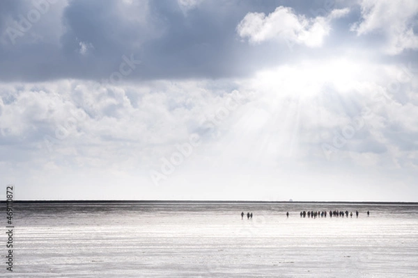 Fototapeta Group of a mudflat hike at low tide in the wide mudflats off Dagebüll in hazy weather with sun rays breaking through the clouds