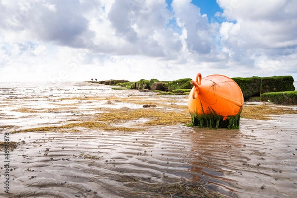 Fototapeta A bright red buoy lies on the mudflat in Dagebüll in Schleswigholstein at low tide