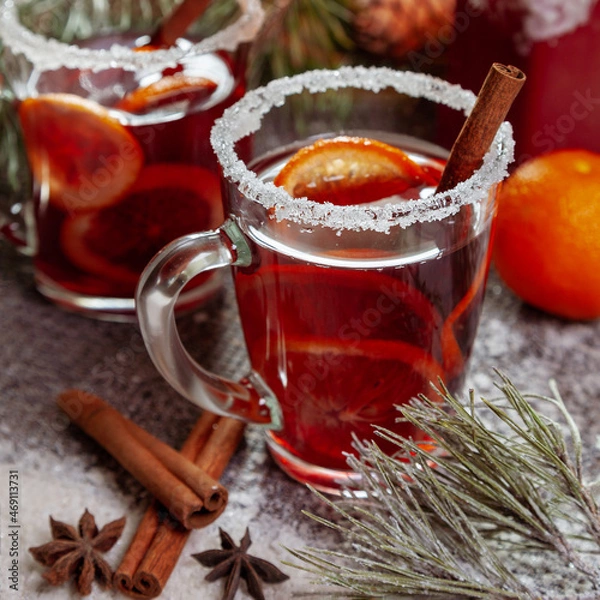 Obraz Christmas hot mulled wine with a slice of orange and spices. A glass cup with a hot traditional drink on a snowy background in festive decorations. Evening mood and decoration 