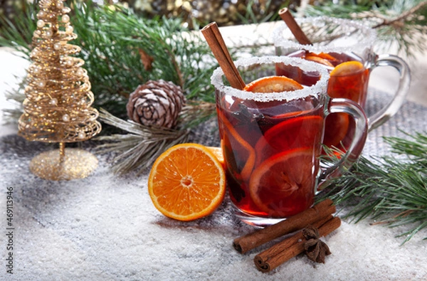 Fototapeta Christmas hot mulled wine with a slice of orange and spices. A glass cup with a hot traditional drink on a snowy background in festive decorations. Evening mood and decoration 