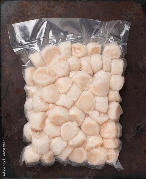 Fototapeta Frozen meat scallop in vacuum package. Raw delicatessen seafood.  dark background. Selective focus, top view and copy space