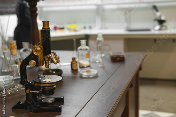 Fototapeta Vintage old microscope on table for science background. Medicine, alchemy, pharmacist. glass jars, flasks and tools, Selective focus