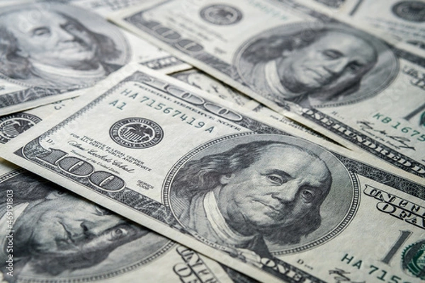 Obraz Part of US 100 american dollar bill with dramatic shadow seen on top of pile of other cash. Selective focus. Concept for finance and investment