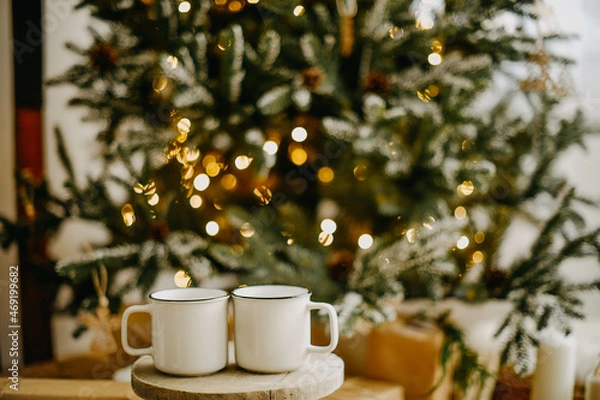 Fototapeta New year 2022, christmas. House room decorated for the holidays. Two cups of tea or coffee on the background of the Christmas tree. Christmas drinks. Warmth and comfort