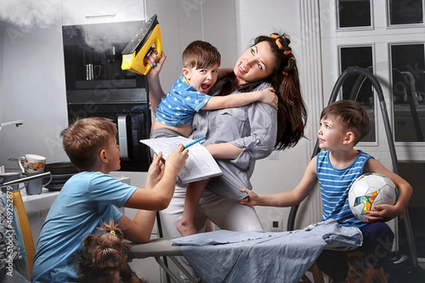 Fototapeta A very busy mother. A very busy woman. A mother who does several things at the same time. A woman who makes several things at the same time. A woman irons and spands time with her children.