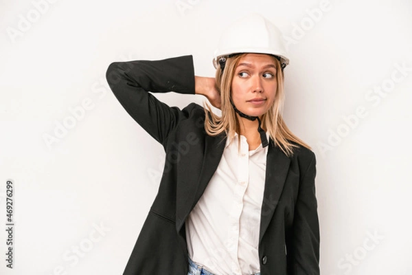 Fototapeta Young caucasian architect woman wearing a helmet isolated on white background touching back of head, thinking and making a choice.