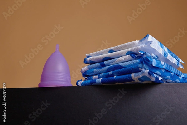 Fototapeta A silicone menstrual cup next to a stack of sanitary towels. Sustainability, zero waste, frugality concept. Alternative way to manage periods, menstrual cycles