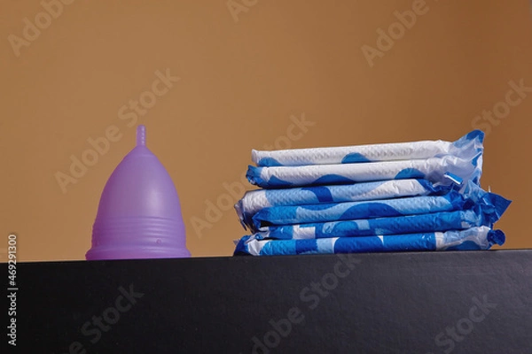 Fototapeta A silicone menstrual cup next to a stack of sanitary towels. Sustainability, zero waste, frugality concept. Alternative way to manage periods, menstrual cycles