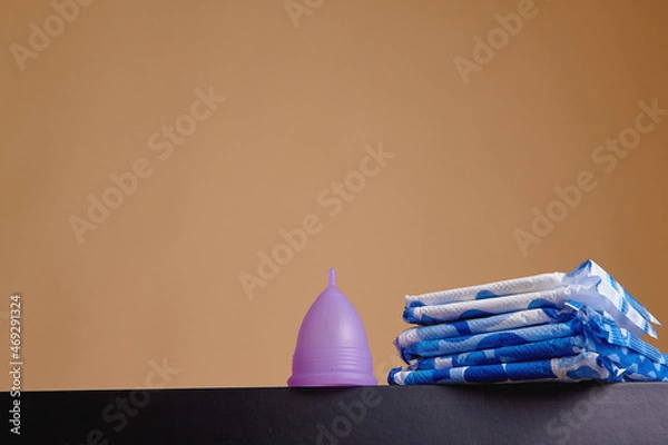 Fototapeta A silicone menstrual cup next to a stack of sanitary towels. Sustainability, zero waste, frugality concept. Alternative way to manage periods, menstrual cycles