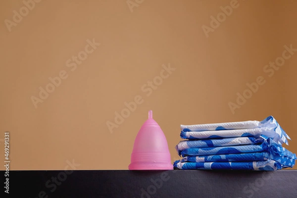 Fototapeta A silicone menstrual cup next to a stack of sanitary towels. Sustainability, zero waste, frugality concept. Alternative way to manage periods, menstrual cycles