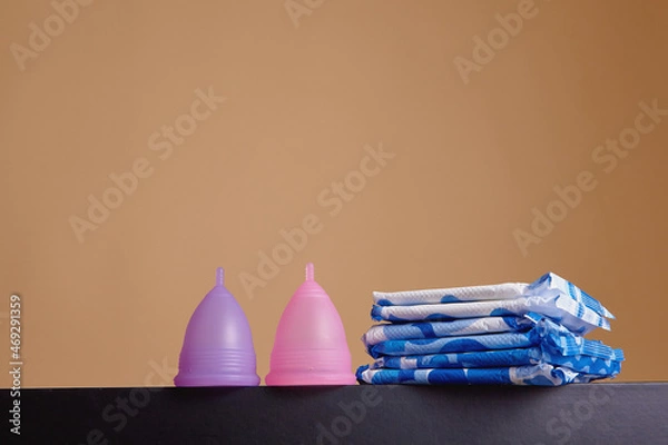 Fototapeta A silicone menstrual cup next to a stack of sanitary towels. Sustainability, zero waste, frugality concept. Alternative way to manage periods, menstrual cycles