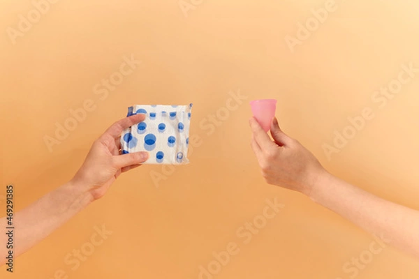 Fototapeta Menstrual cup and sanitary pad in hands. Feminine hygiene alternative product instead of tampon during her period. Menstruation, critical days, zero waste, eco, ecology concept.