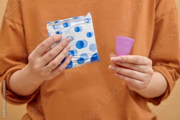 Fototapeta Menstrual cup and sanitary pad in hands. Feminine hygiene alternative product instead of tampon during her period. Menstruation, critical days, zero waste, eco, ecology concept.