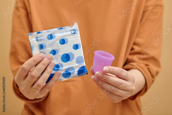 Fototapeta Menstrual cup and sanitary pad in hands. Feminine hygiene alternative product instead of tampon during her period. Menstruation, critical days, zero waste, eco, ecology concept.
