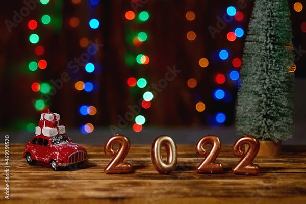 Fototapeta Holiday background  Numbers of year 2022 made by gold candles on bokeh festive sparkling background. celebrating New Year holiday, close-up. Space for text
