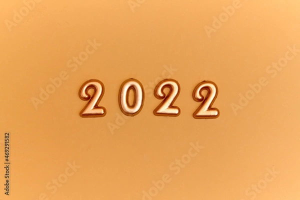 Fototapeta Holiday background  Numbers of year 2022 made by gold candles on bokeh festive sparkling background. celebrating New Year holiday, close-up. Space for text