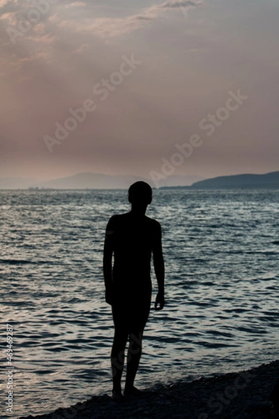 Fototapeta Contemporary art dramatic portrait silhouette a man at the sea in rays of the setting sun against the backdrop dark waves and beautiful evening sky