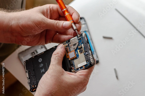 Fototapeta A man is repairing a Smartphone. Hands hold a screwdriver and di