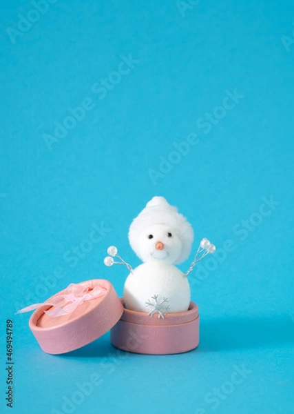 Fototapeta White snowman with snowflake in pink present box against pastel blue background. Winter holidays and New Year gift concept.