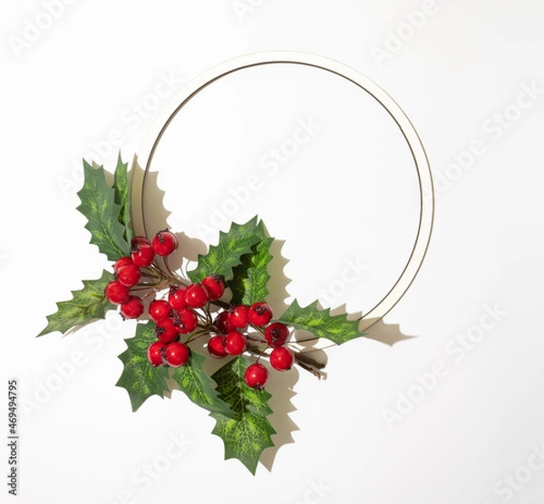Obraz Christmas round frame with christmas red berries and green leaves on white background. Sunny shadow and copy space. Winter holidays and New Year composition.