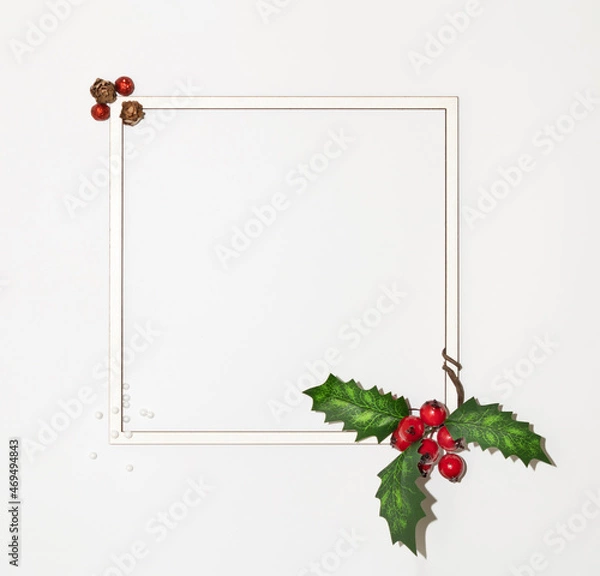 Fototapeta Christmas square frame with paper card space with winter red berries with green leaves and ornaments on white background. Minimal winter holidays and New Year layout.