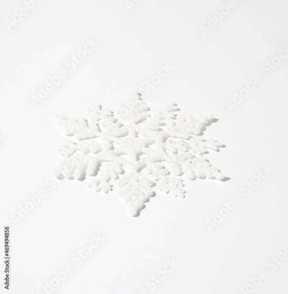 Fototapeta Christmas white snowflake with sparkle on white table. Minimal winter holidays and New Year monochrome aesthetic background.