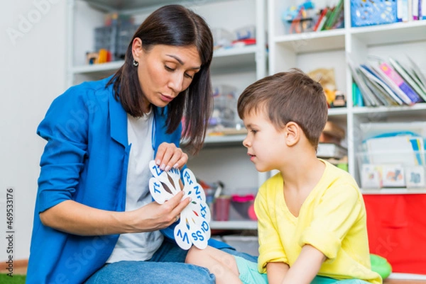 Obraz A cute boy with a speech therapist is taught to pronounce the letters, words and sounds.