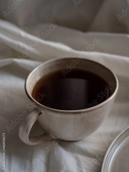Fototapeta Breakfast in bed, a cup of black tea and thin pancakes with currant jam and sour cream on a beige ceramic plate on a soft white bed in the morning light