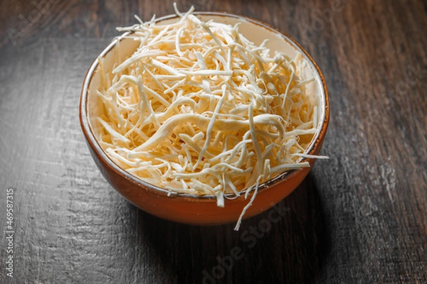 Fototapeta Fibrous chechil cheese in a deep cup stands on a wooden table.