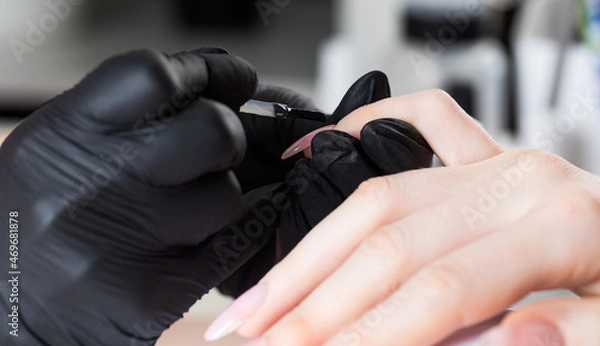 Obraz Manicure process in a beauty salon. The manicurist paints the nail with varnish.